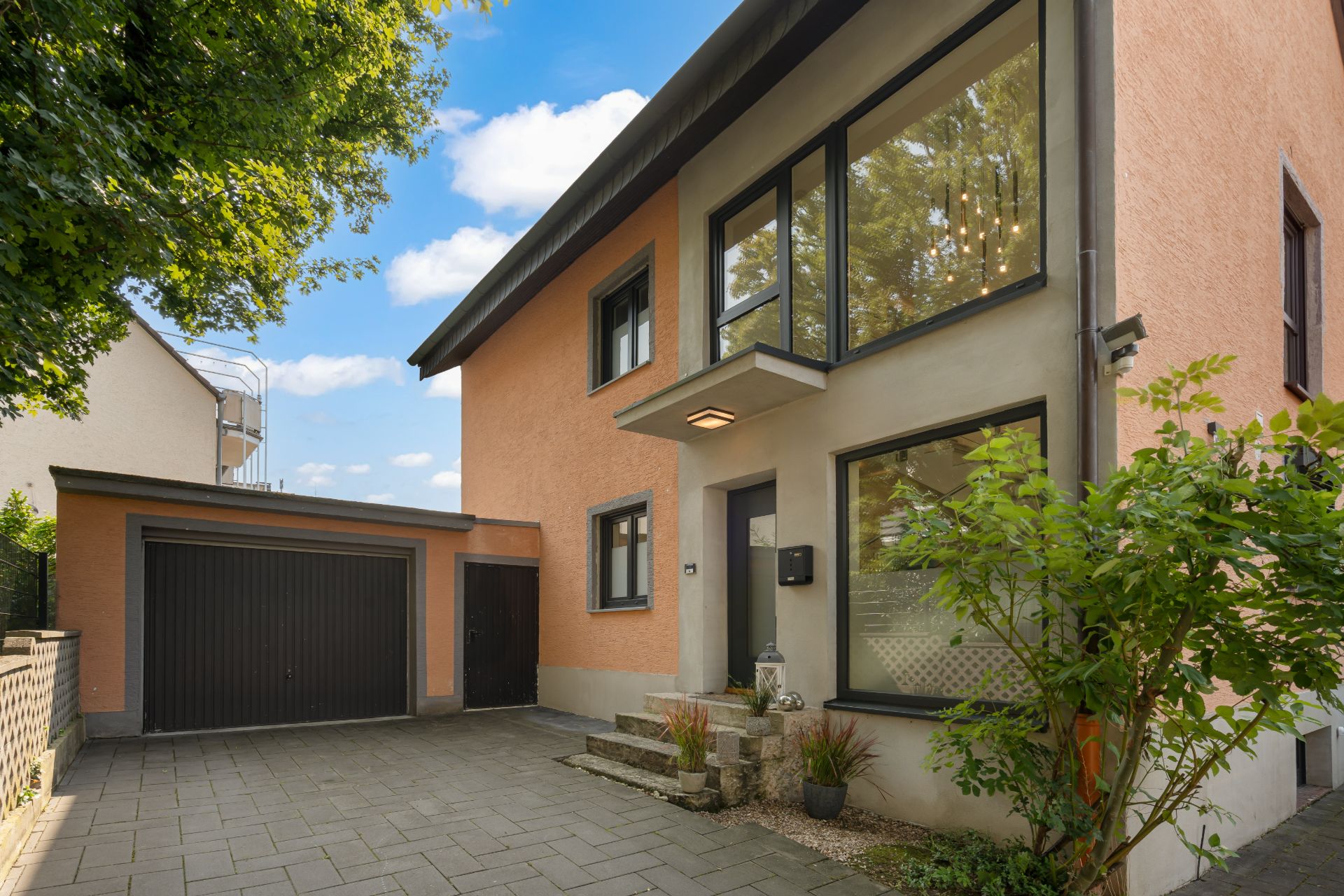 Modernes Wohnhaus mit großem Fenster, Eingangsstufen und angrenzender Garage.