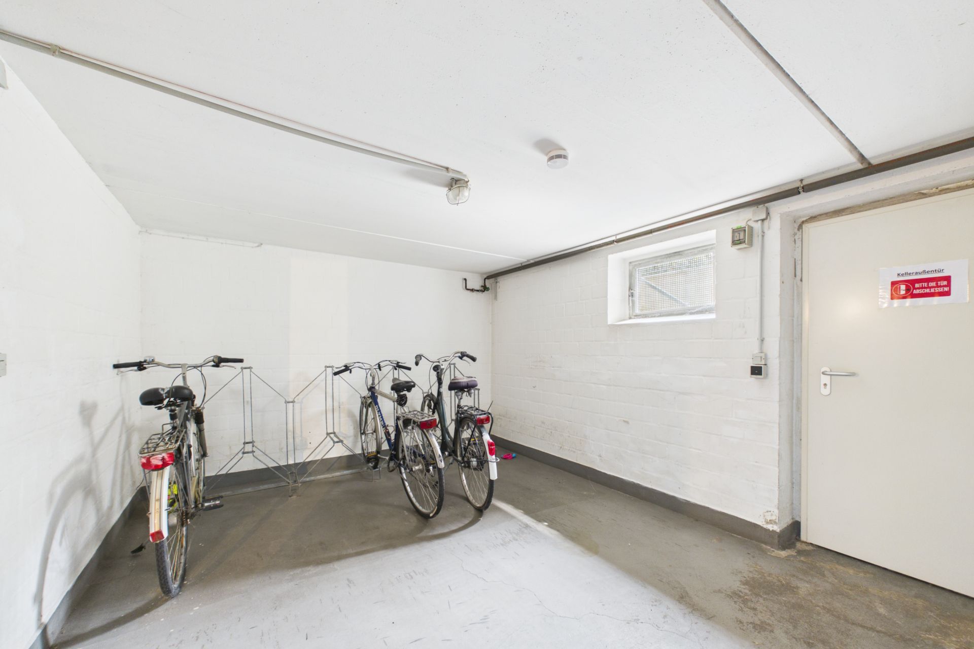 Heller Kellerraum mit vier abgestellten Fahrrädern und einem Fahrradständer.