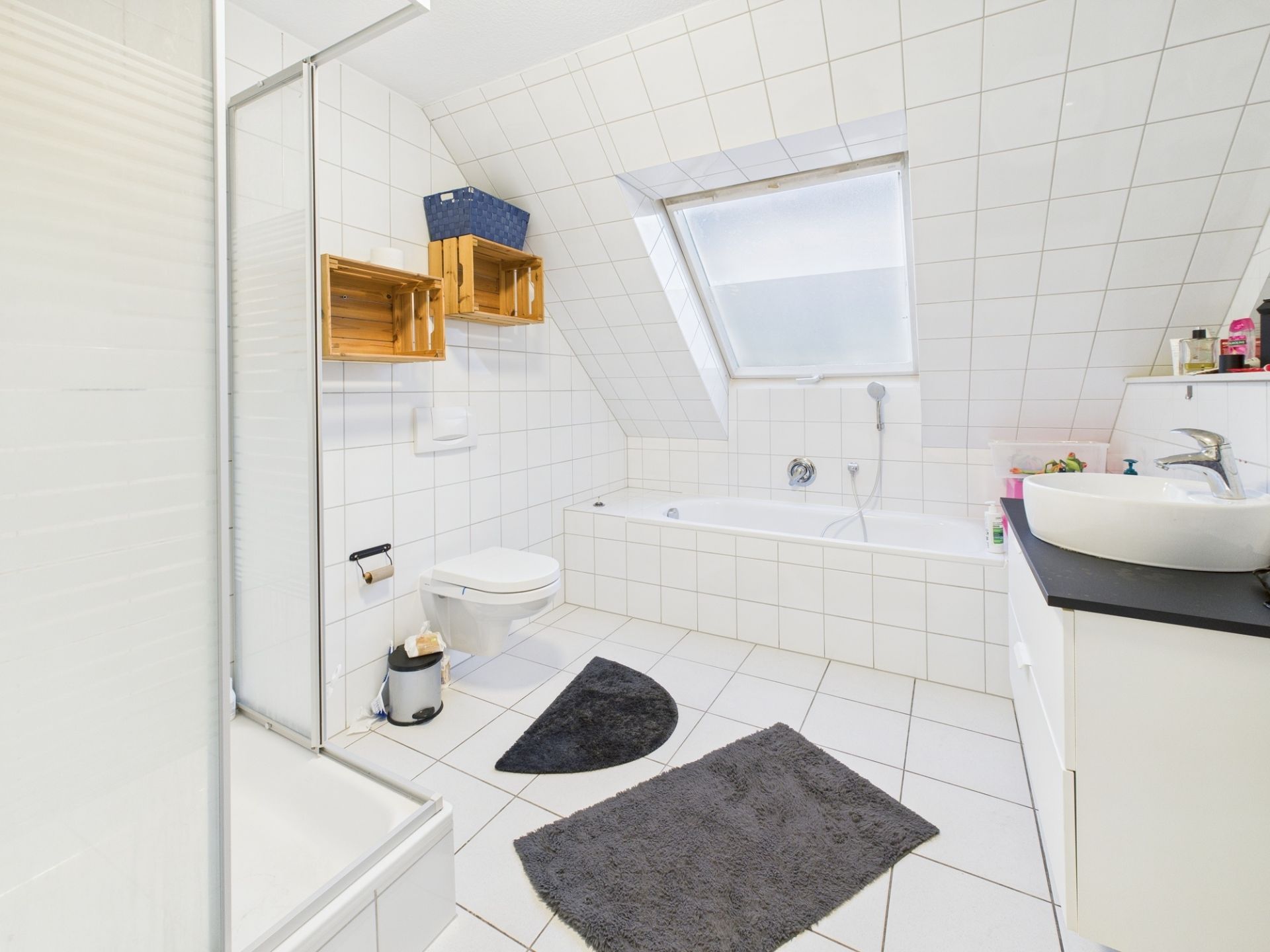 Helles, gefliestes Badezimmer mit Dusche, Badewanne, Toilette, Waschbecken und Dachfenster.