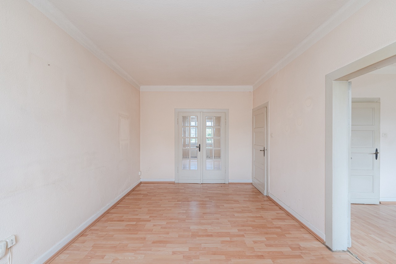 Leerer Raum mit hellem Laminatboden, weißen Türen und hellen Wänden.