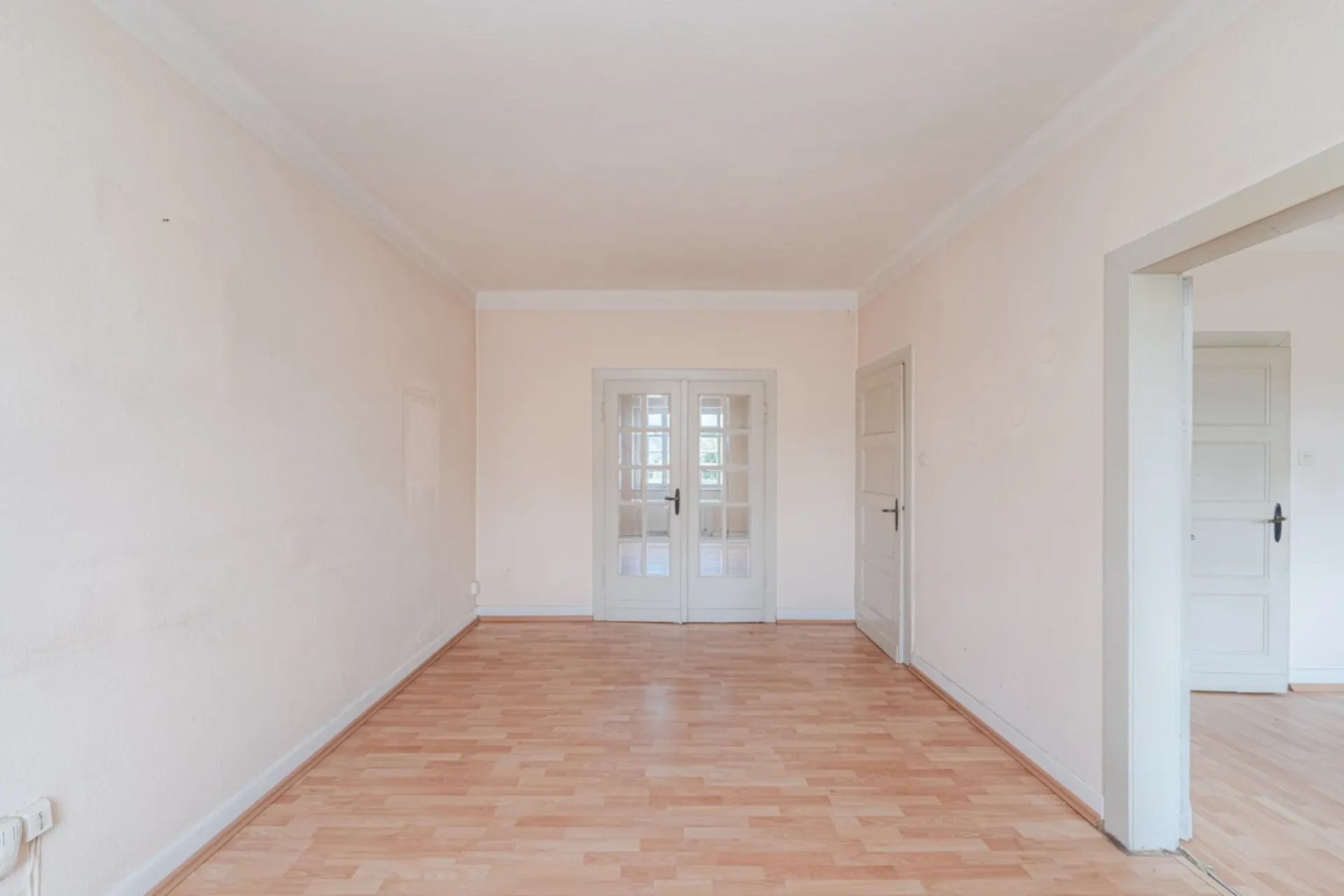 Leerer Raum mit hellem Laminatboden, weißen Türen und hellen Wänden.