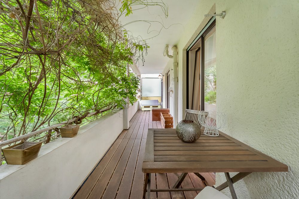 Langer Balkon mit Holzfußboden, Tisch, Stühlen und grünen Pflanzen an der Seite.