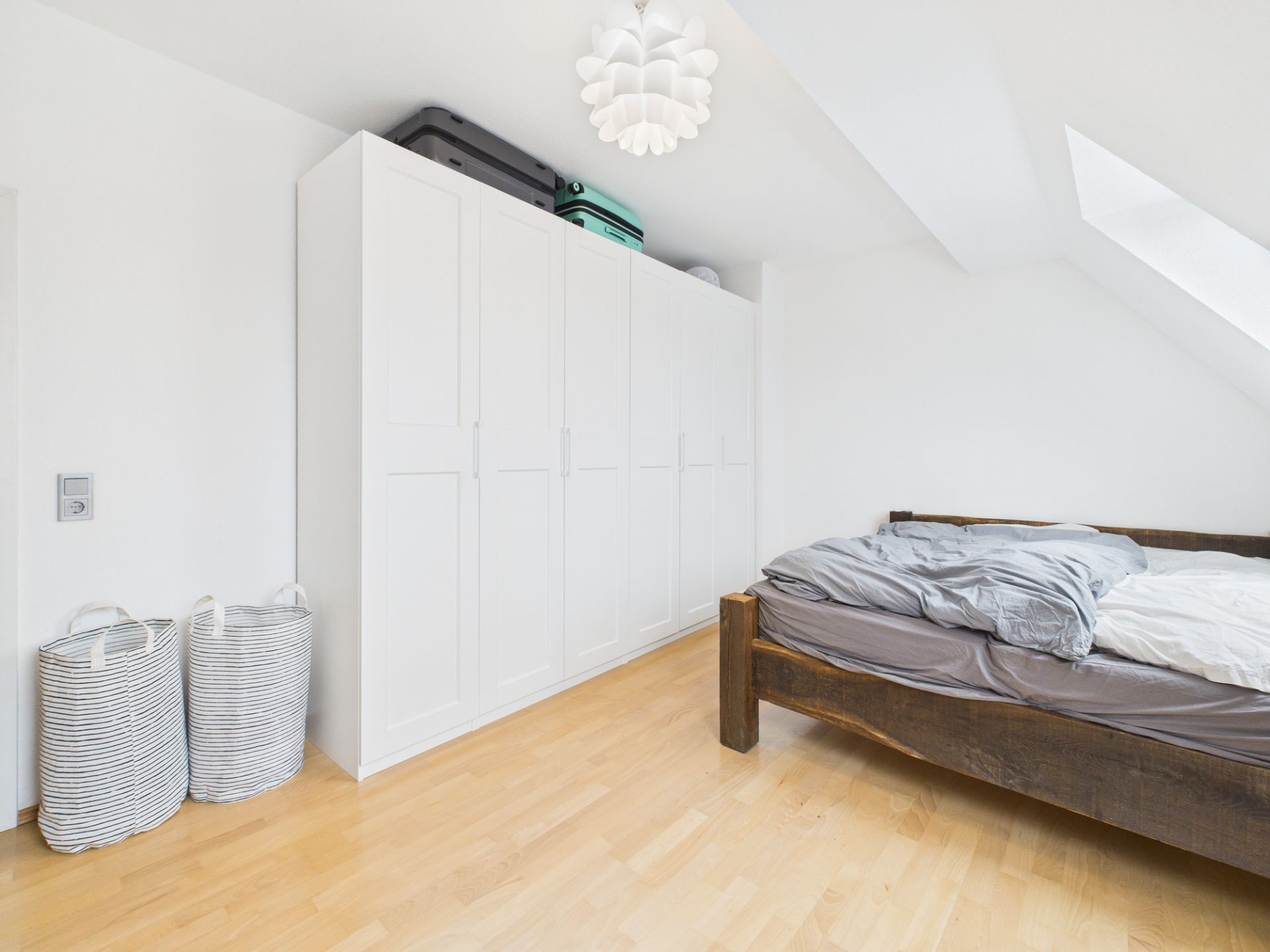 Helles Schlafzimmer mit großem weißen Kleiderschrank, einem Holzbett und zwei Wäschekörben.