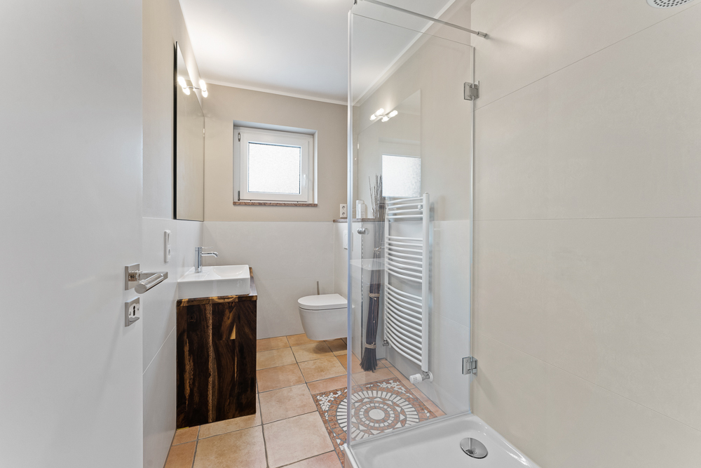 Modernes Badezimmer mit Dusche, WC, Waschbecken, Handtuchheizkörper und Fenster.