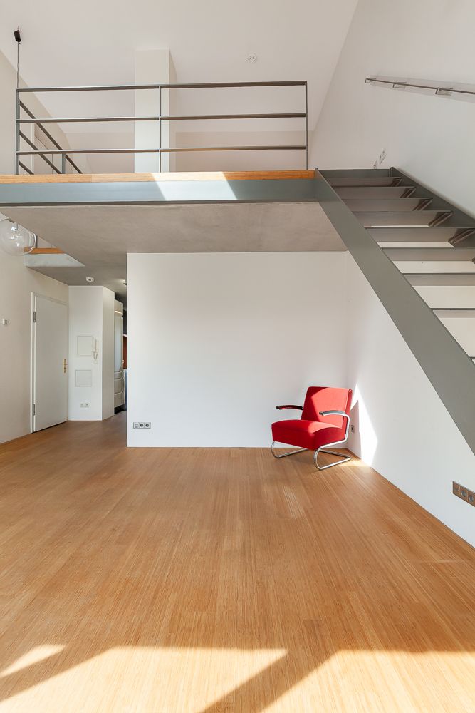 Zimmer mit Holzfußboden, rotem Sessel, Treppe und Galerieebene.