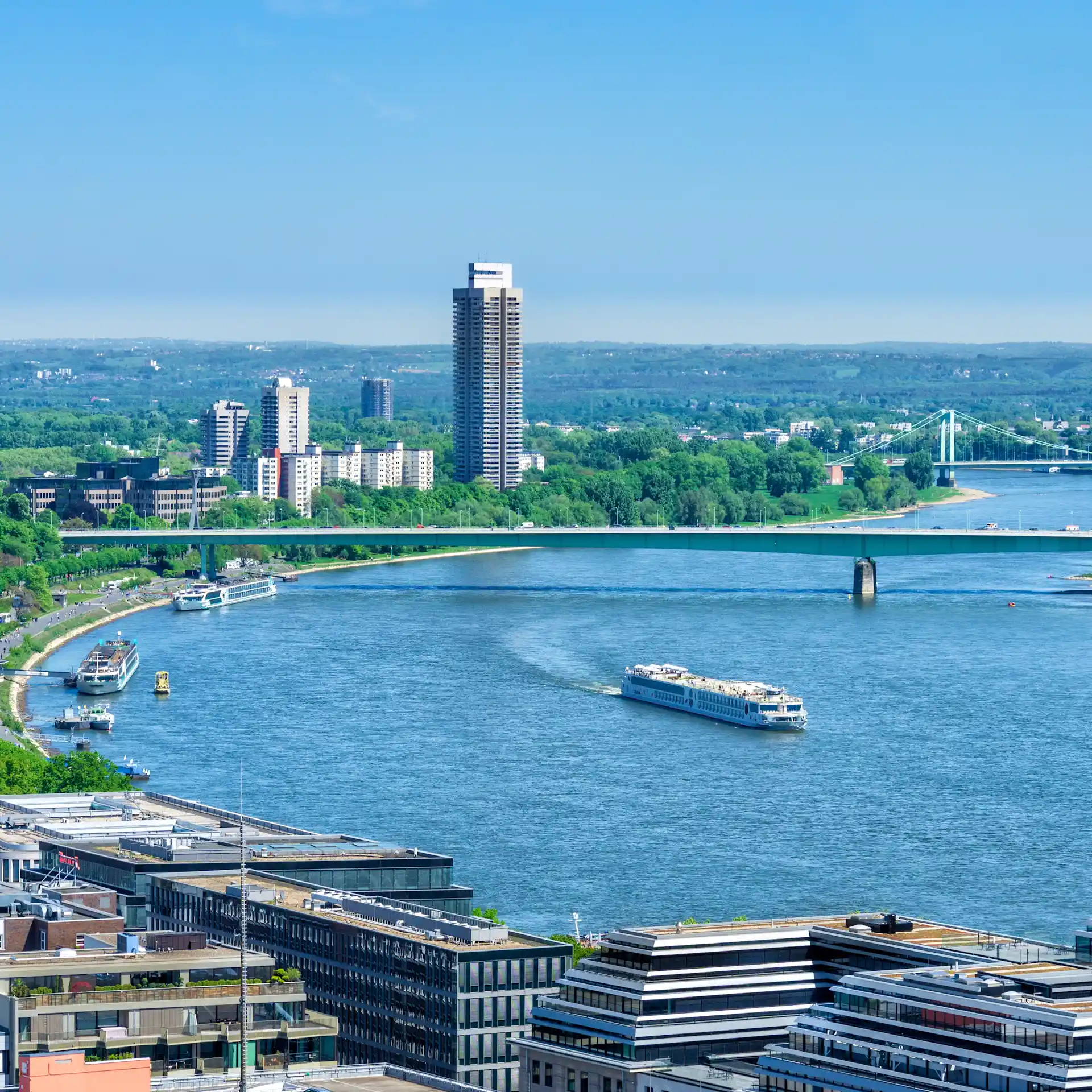 Blick auf einen Fluss mit moderner Uferbebauung, Brücken und Schiffen bei klarem Himmel.