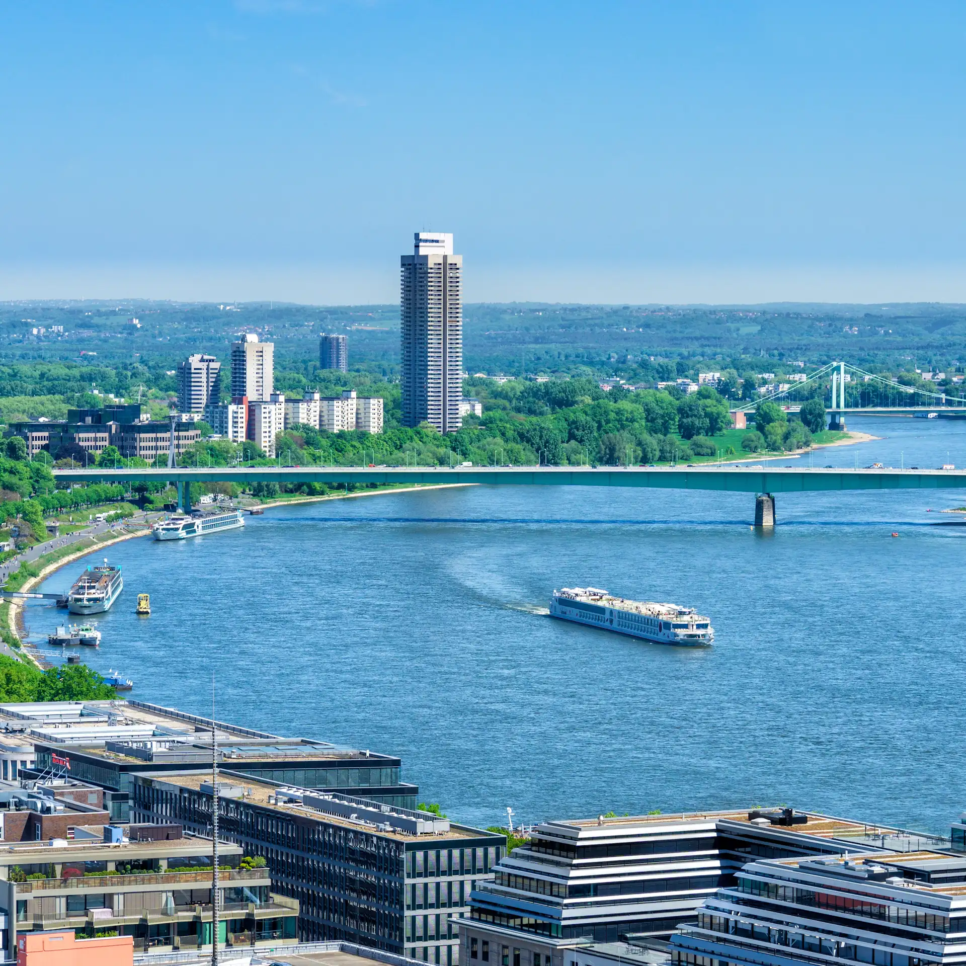 Blick auf einen Fluss mit moderner Uferbebauung, Brücken und Schiffen bei klarem Himmel.