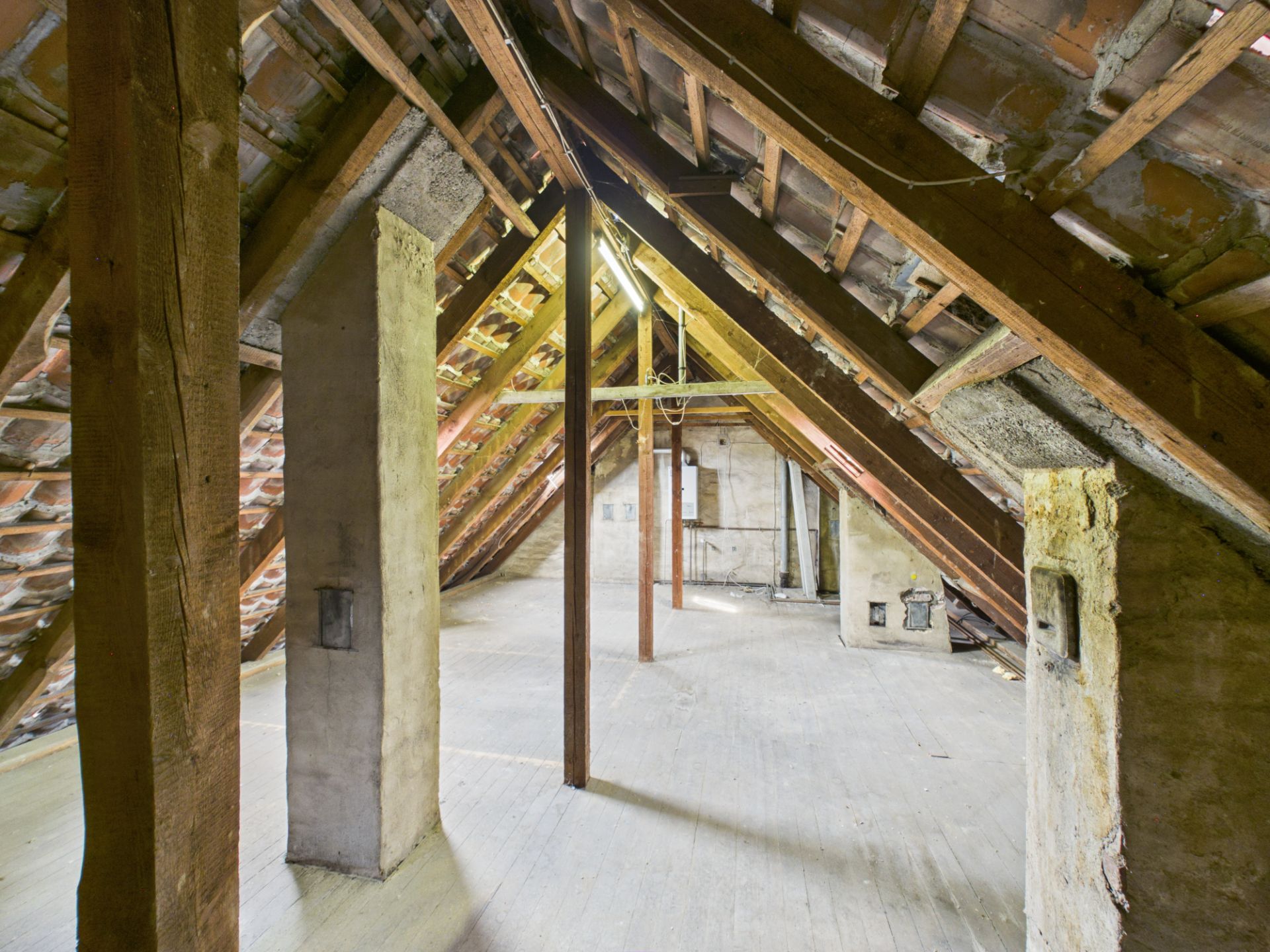 Dachboden mit sichtbaren Holzbalken und Betonpfeilern, unbeheizt und leer.