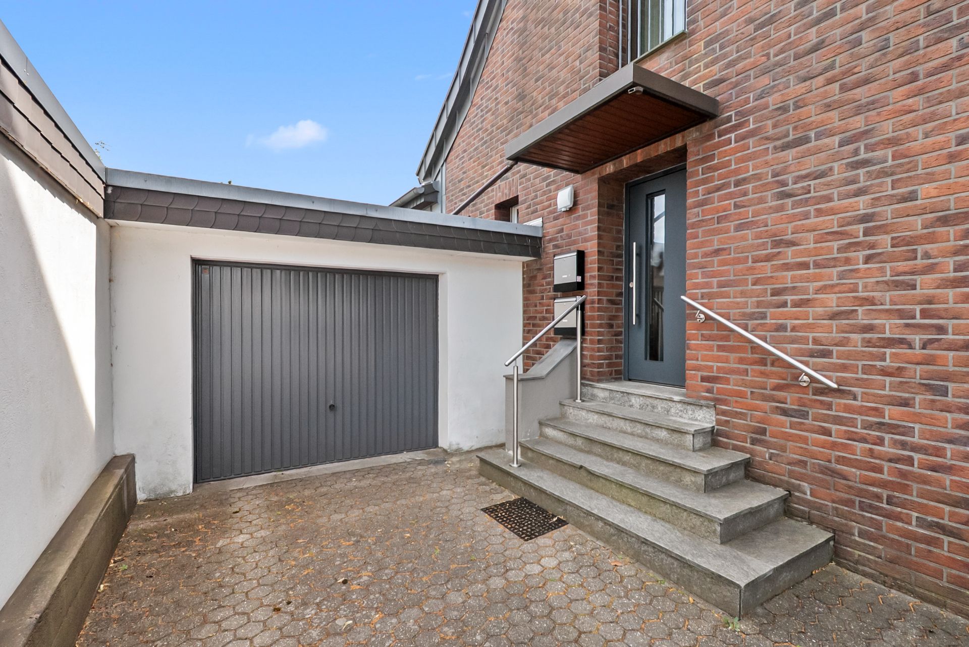 Eingangsbereich mit Treppe, Haustür und angrenzender Garage in einem Innenhof.