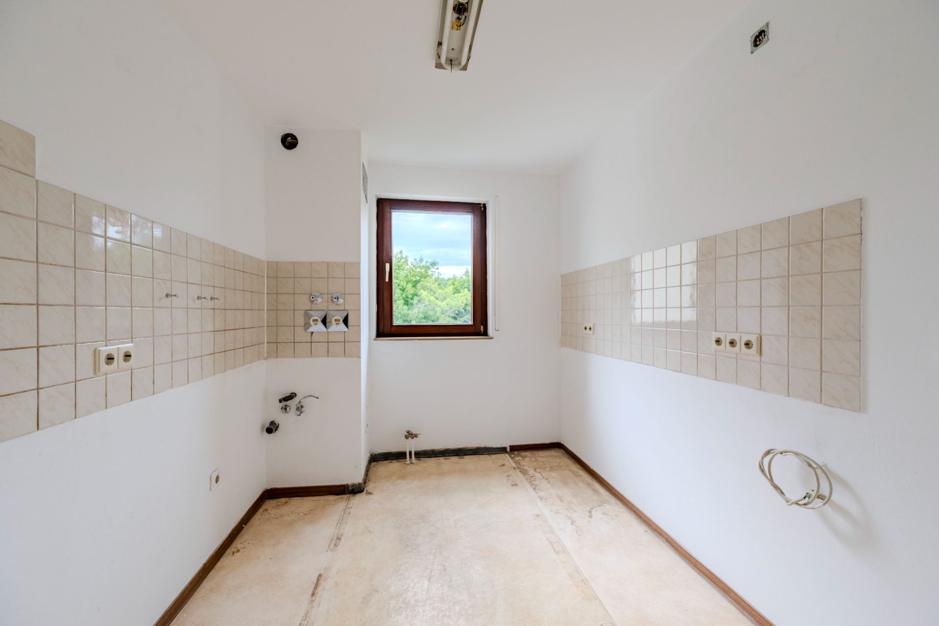 Leerer, schmaler Raum mit weißen Wänden, Fliesen und einem Fenster in der Mitte.