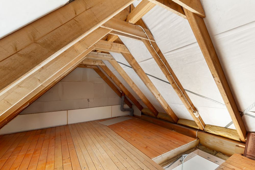 Unfertiger Dachboden mit Holzbalken und Holzfußboden, sichtbarer Dachstuhl.