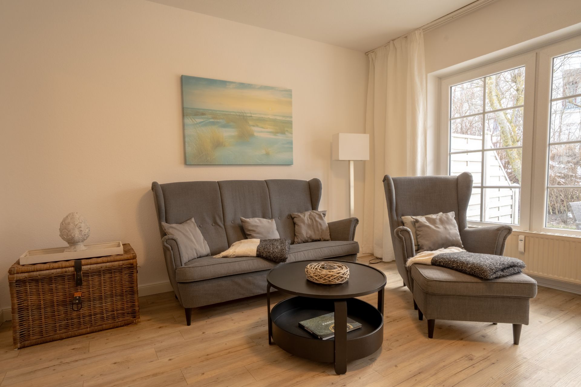 Helles Wohnzimmer mit grauem Sofa, Sessel, Couchtisch und großem Fenster.