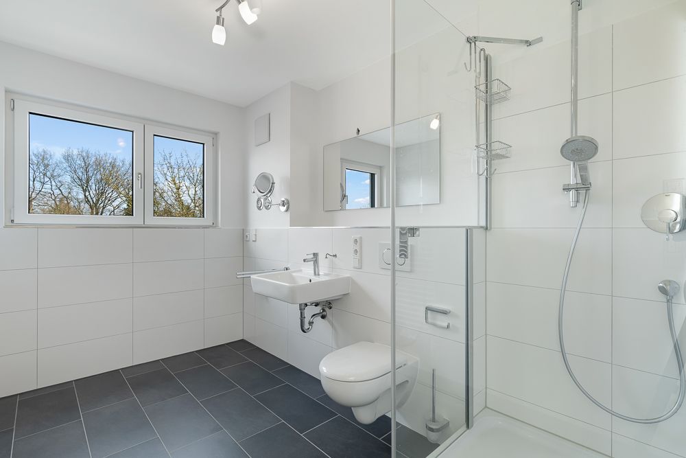 Helles Badezimmer mit Dusche, WC, Waschbecken und Fenster.
