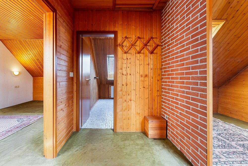Flur mit Holzvertäfelung, grüner Teppich, Garderobe und Zugang zu drei Räumen, darunter einer mit Backsteinwand.
