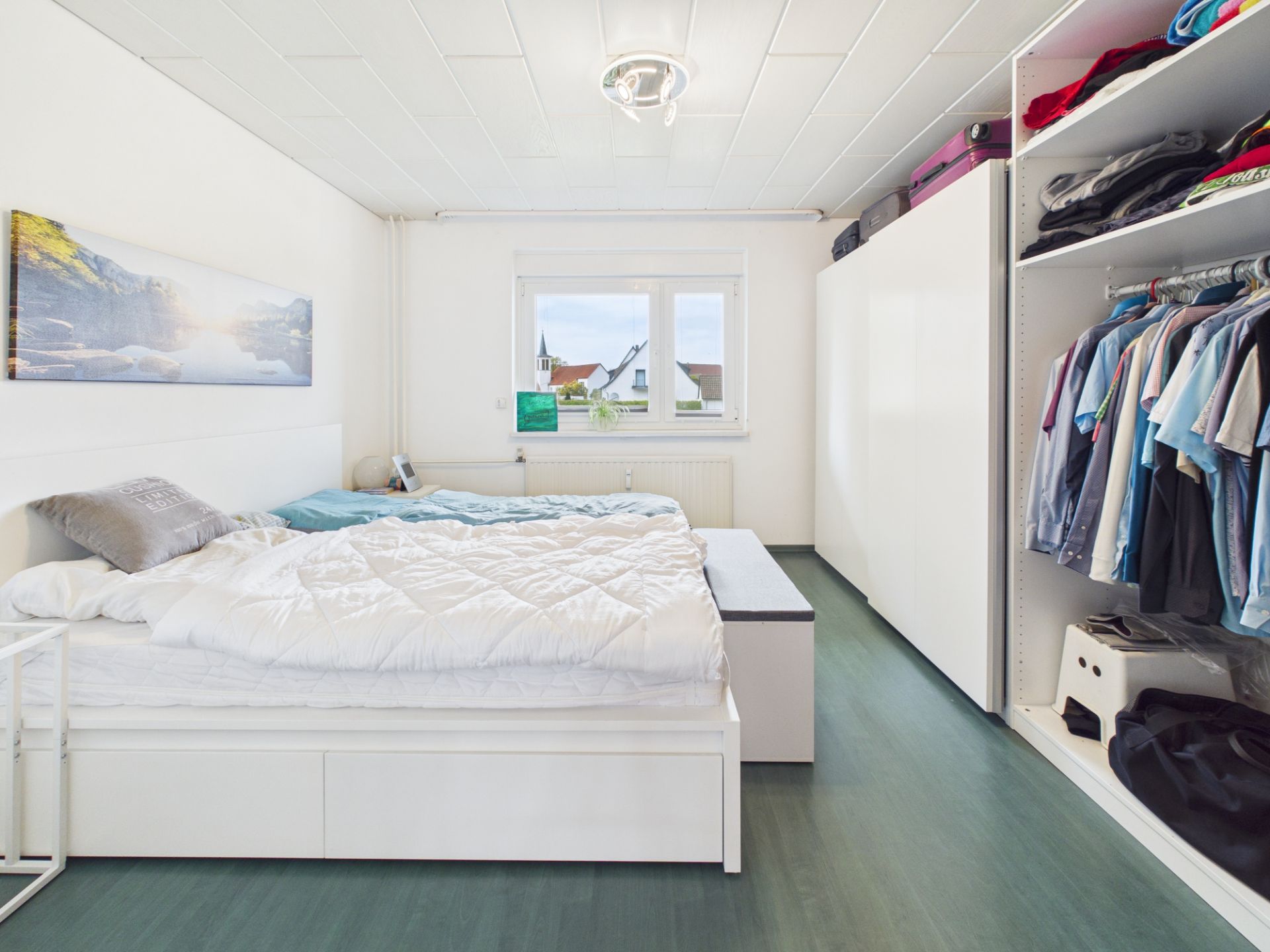 Helles Schlafzimmer mit Doppelbett, großem Kleiderschrank und Fenster mit Blick nach draußen.