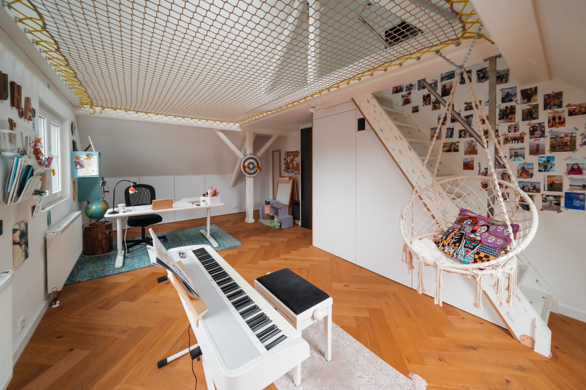 Helles Zimmer mit Schreibtisch, Hängekorb, Keyboard, Fotos an der Wand und Netz an der Decke.