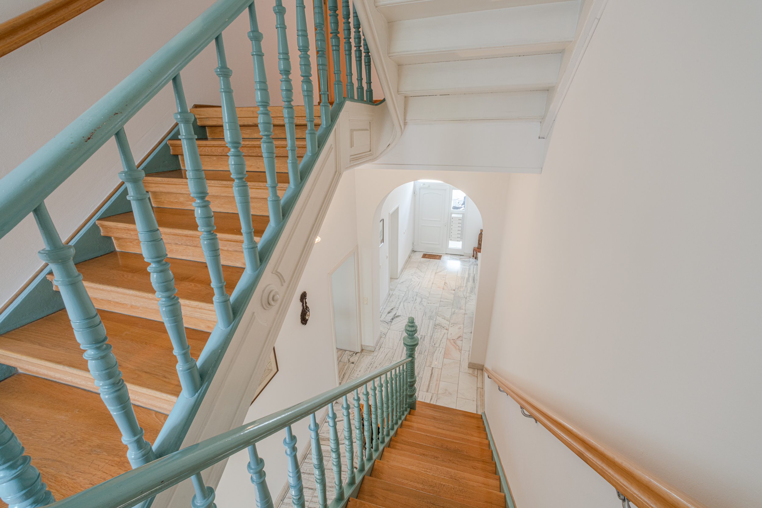 Holztreppe mit blauem Geländer in einem hellen Flur mit Marmorboden.