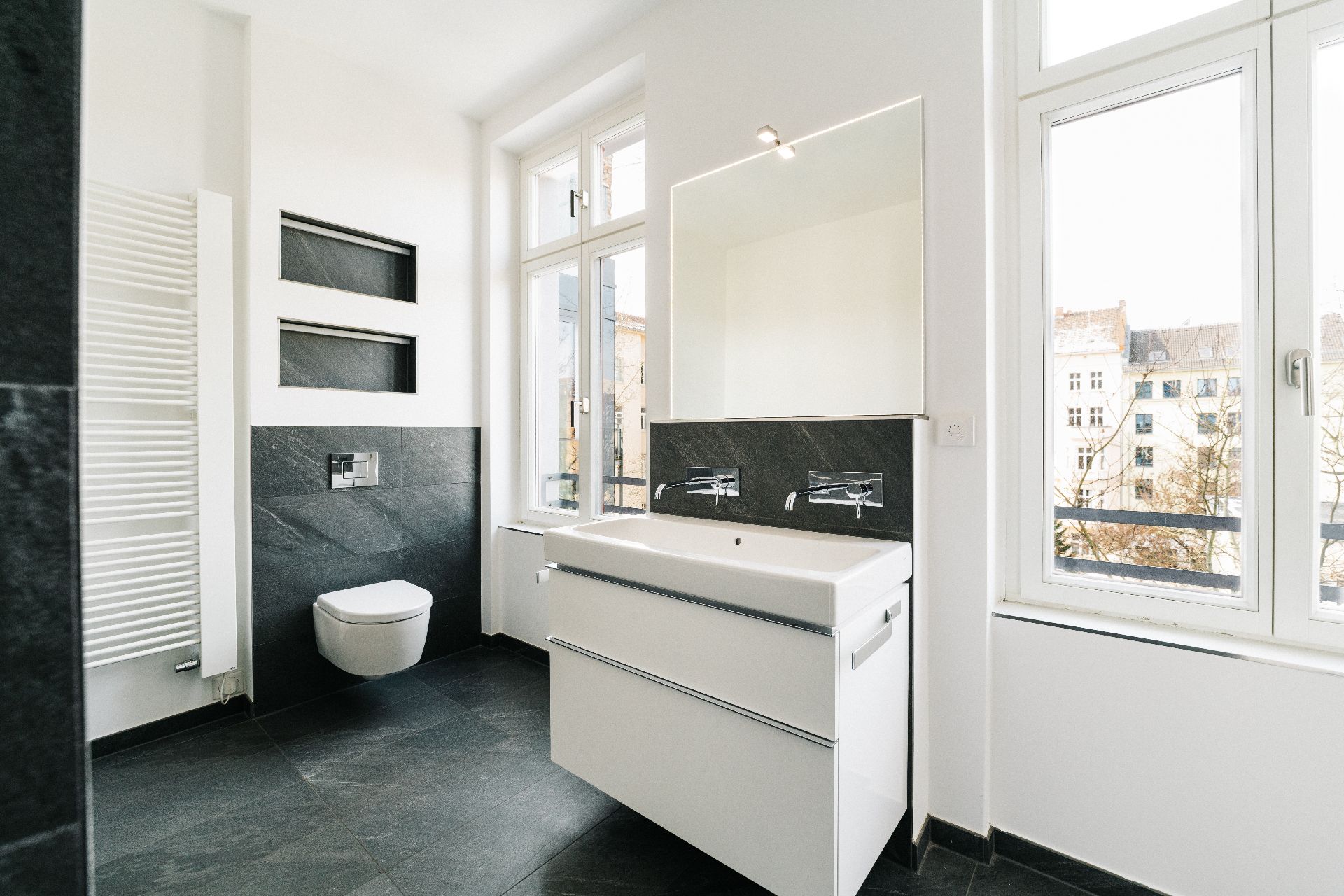 Modernes Badezimmer mit großem Fenster, Doppelwaschbecken und Wandtoilette.