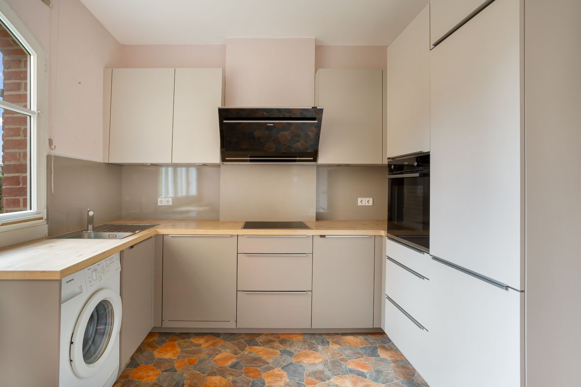 Moderne Einbauküche mit Waschmaschine, Herd, Backofen und hellem Holz-Arbeitsbereich.