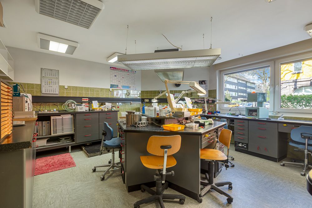 Helles Arbeitszimmer mit mehreren Schreibtischen, Stühlen und großen Fenstern im Hintergrund.