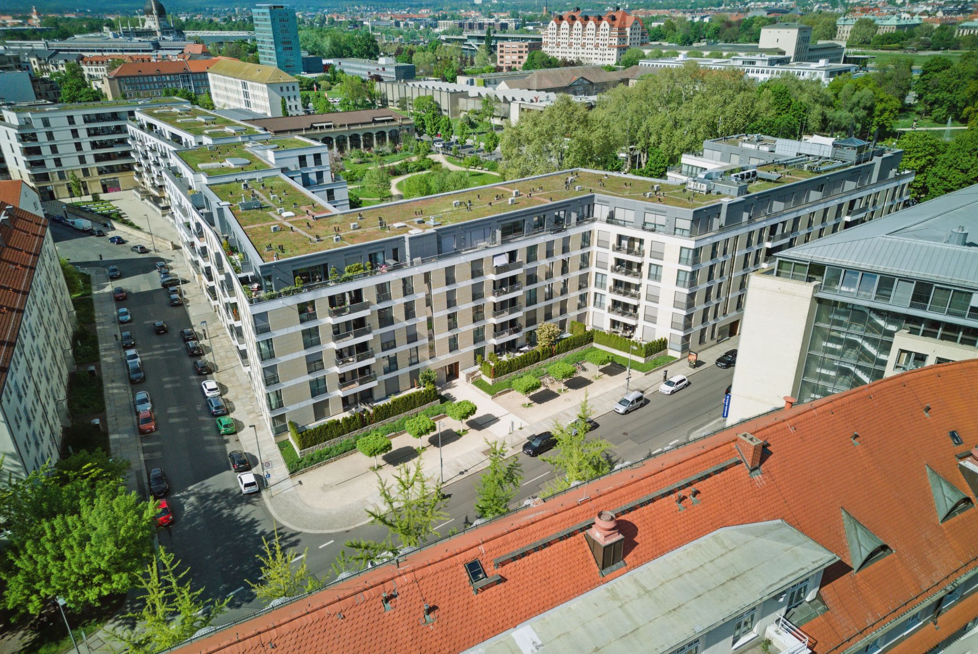 Großes, modernes Wohngebäude mit begrünten Flachdächern an einer Straßenecke, umgeben von weiteren Häusern.