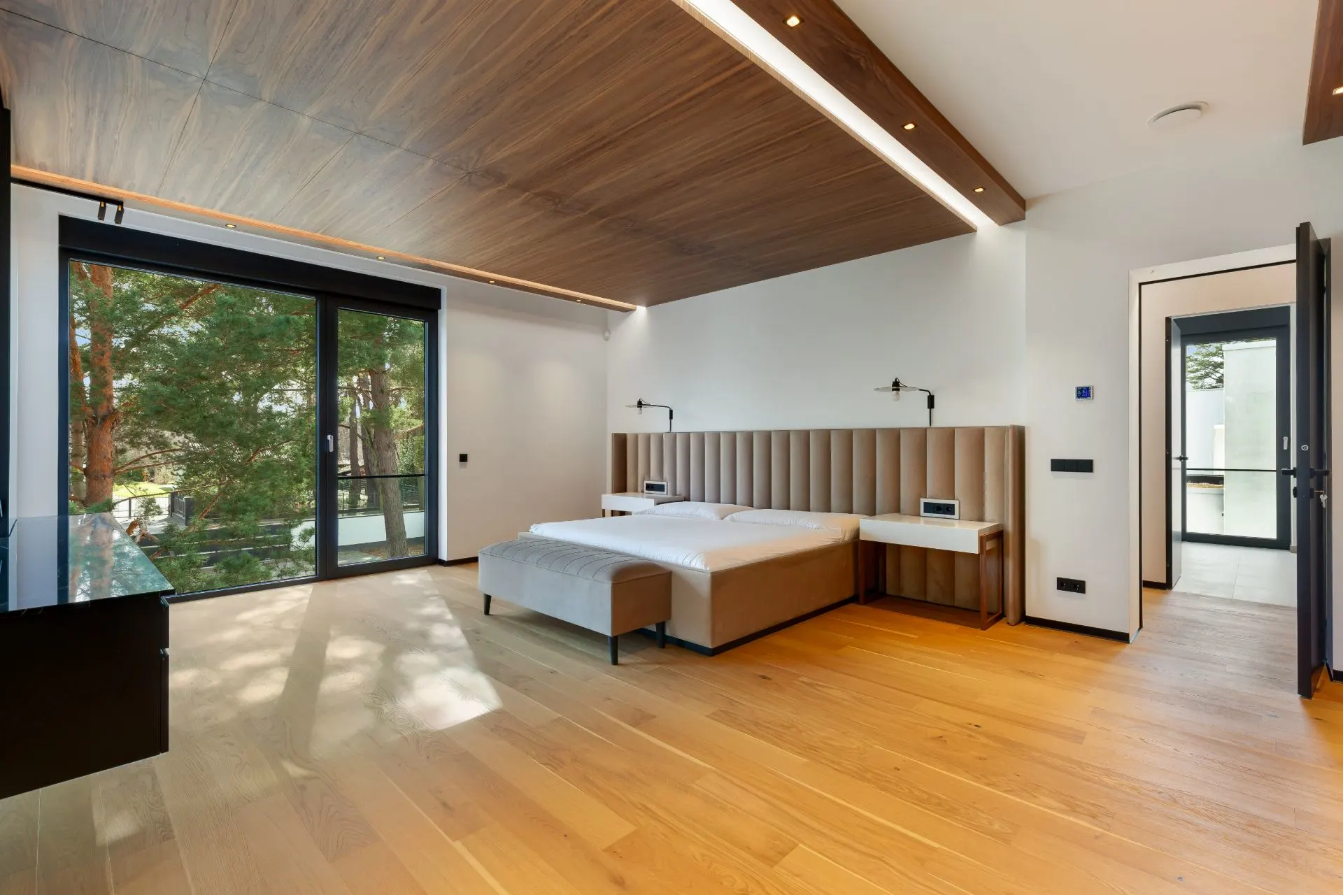 Modernes Schlafzimmer mit Doppelbett, Holzfußboden und großem Fenster mit Blick ins Grüne.