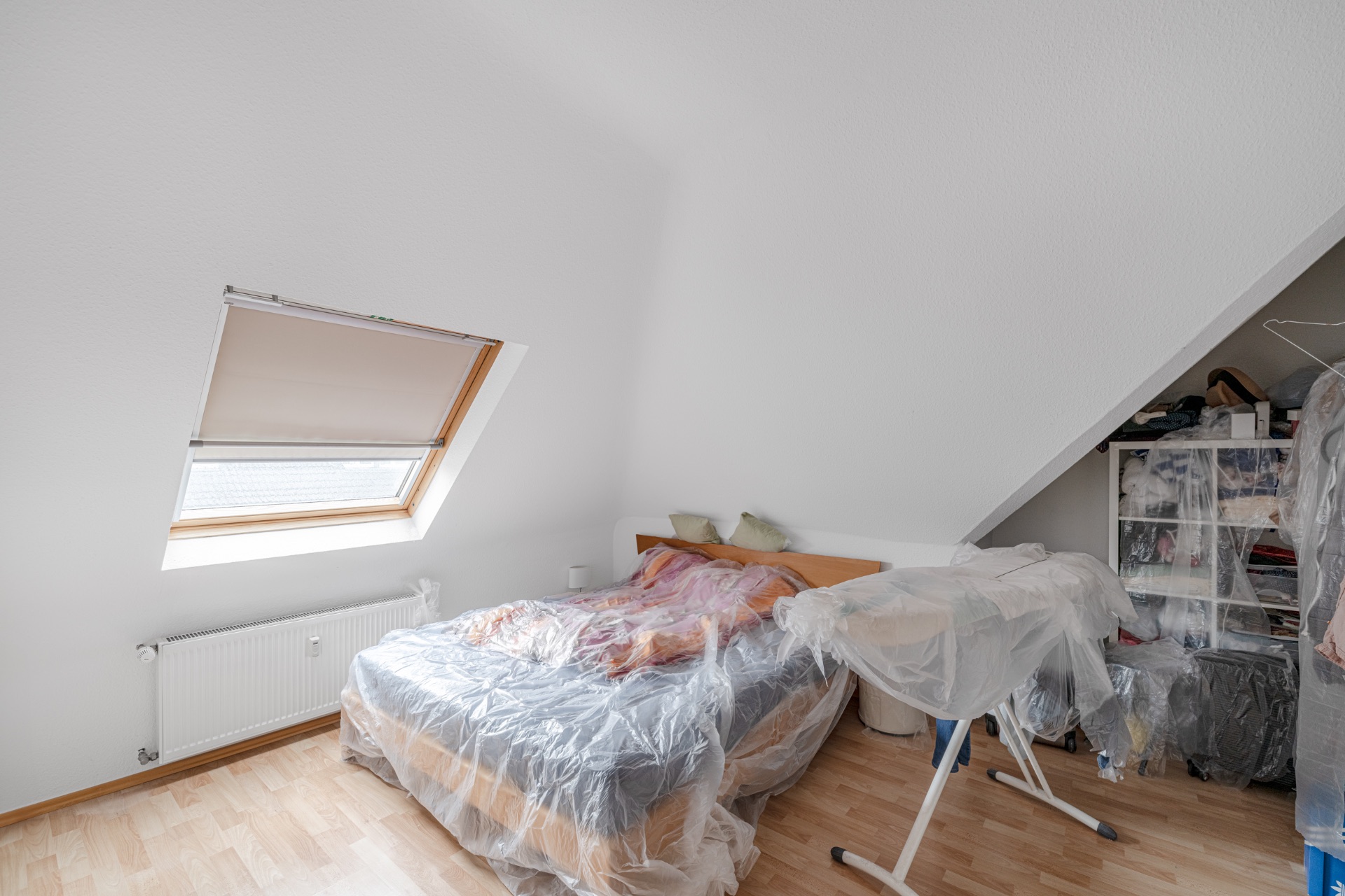 Schlafzimmer mit Dachfenster, Bett und Möbeln, alle mit Plastikfolie abgedeckt.