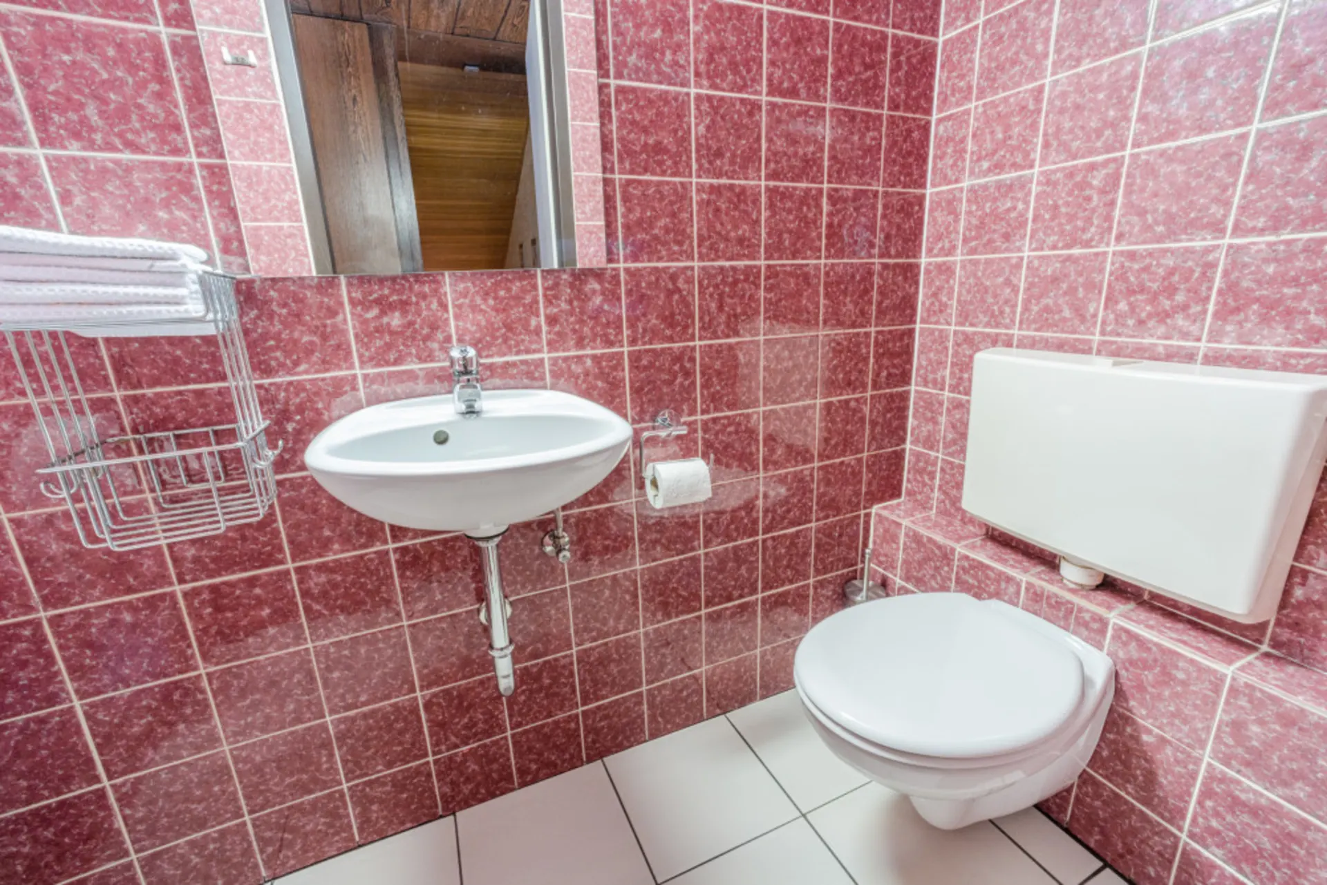 Kleines Badezimmer mit rotem Fliesenspiegel, Waschbecken und Wandtoilette.