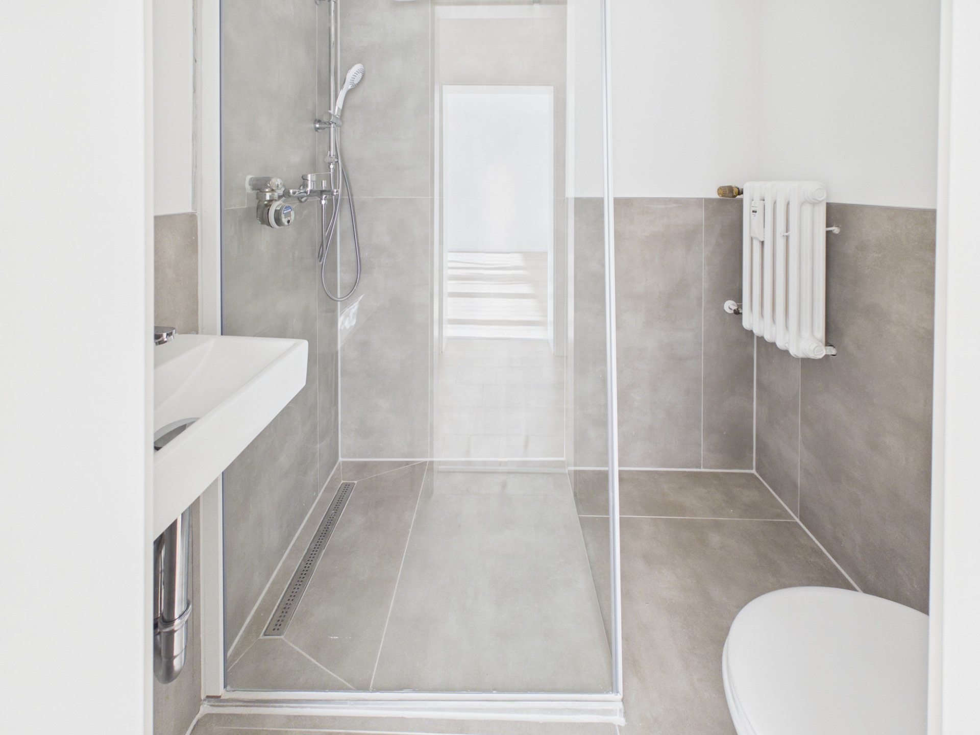 Modernes, helles Badezimmer mit Dusche, Waschbecken, WC und Heizkörper.