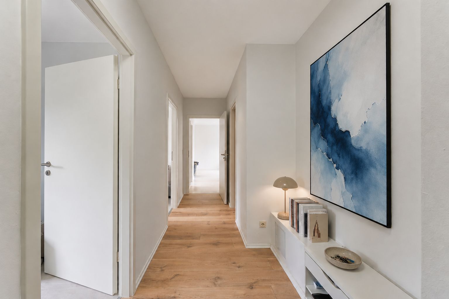Heller Flur mit Holzfußboden, großem abstraktem Bild und Regal mit Dekoration an der Wand.