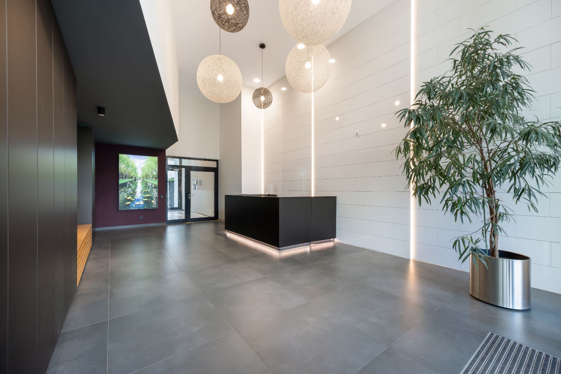 Modernes Foyer mit dunklem Empfangstresen, großen Lampen und einer großen Pflanze im Topf.