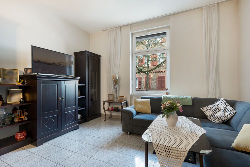 Wohnzimmer mit Ecksofa, Couchtisch, Fernseher auf Schrank und Fenster mit Blick nach draußen.