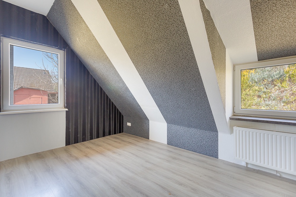Helles Zimmer mit Dachschräge, zwei Fenstern und hellem Laminatboden.