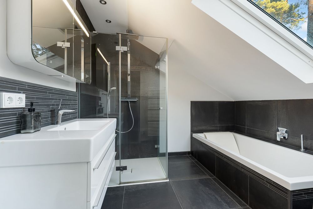 Modernes Badezimmer mit Dusche, Badewanne und großem Fenster im Dachgeschoss.