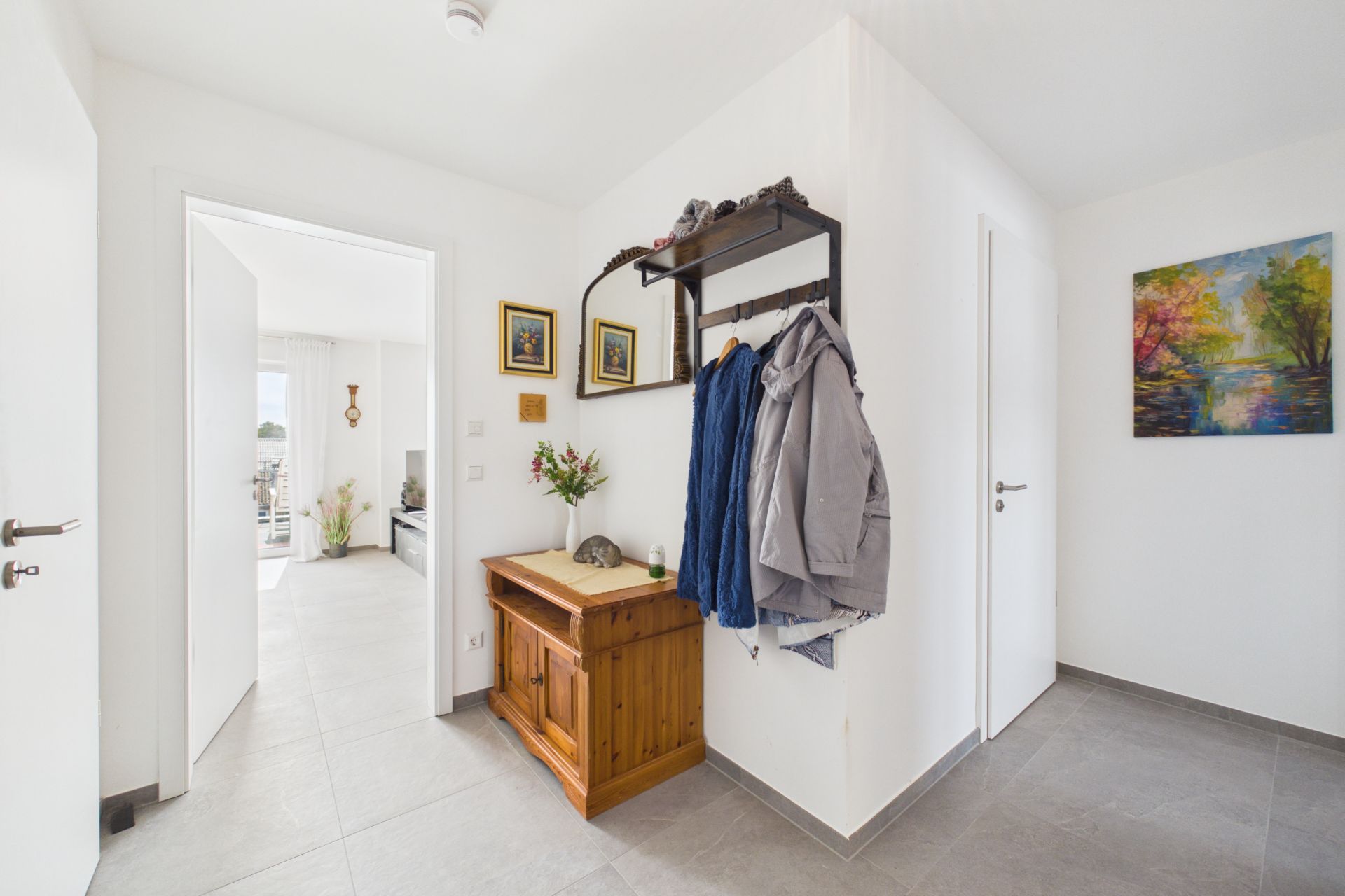 Heller Flur mit Garderobe, Sitzbank, Jacken, Bildern und Zugang zu weiteren Räumen.