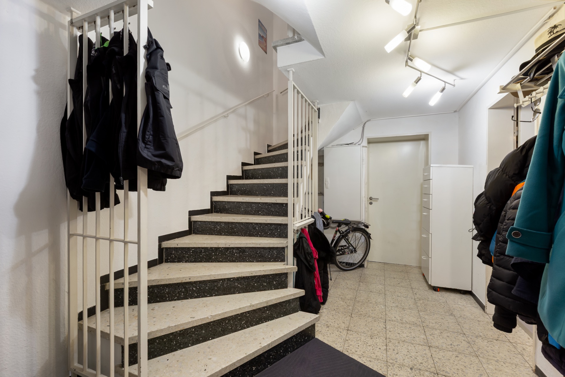 Eingangsbereich mit Treppe, Garderobe, Fahrrad und Jacken an der Wand.