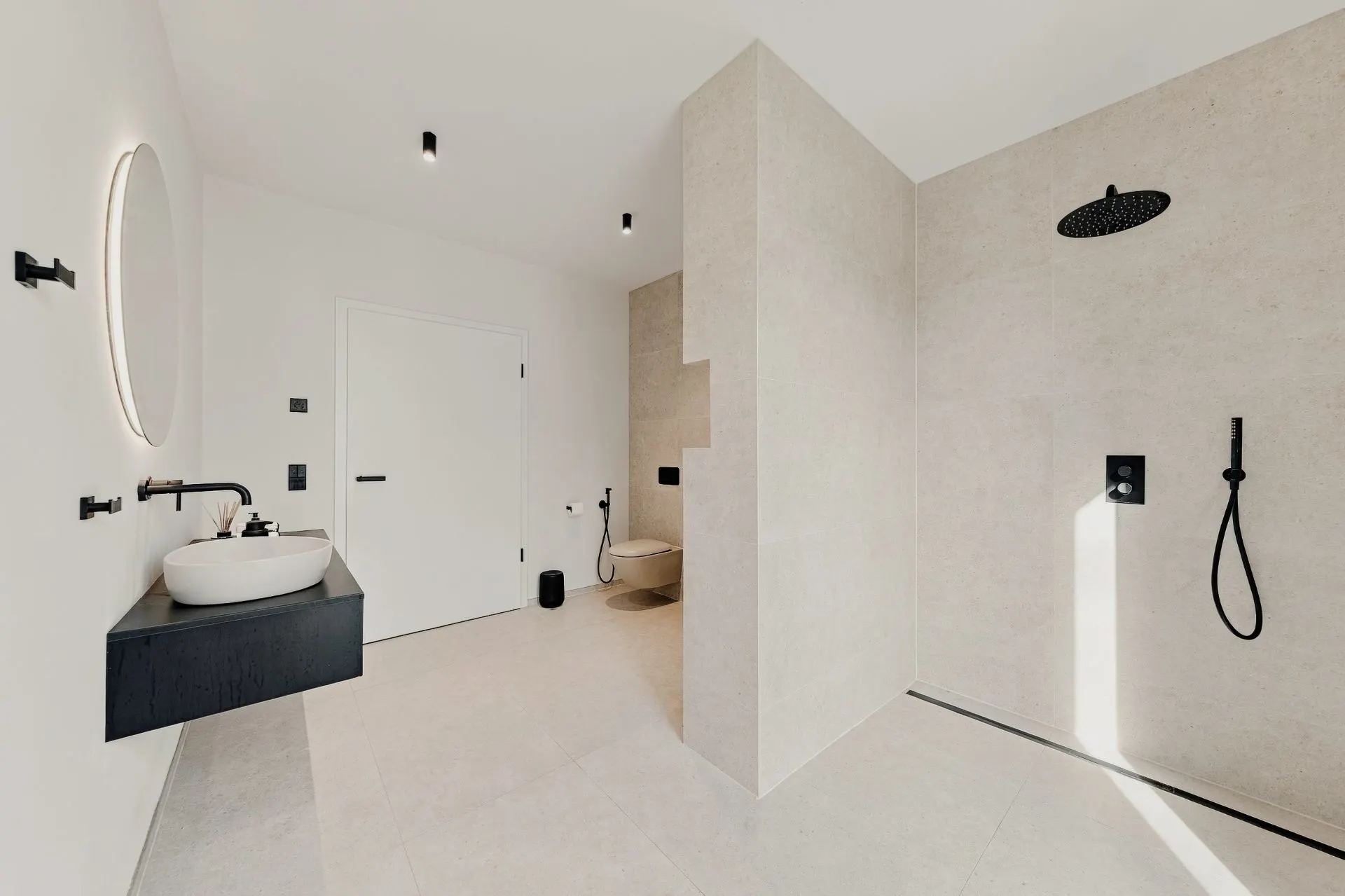 Modernes Bad mit Dusche, Waschbecken, Spiegel und WC, alles in neutralen Farben gehalten.