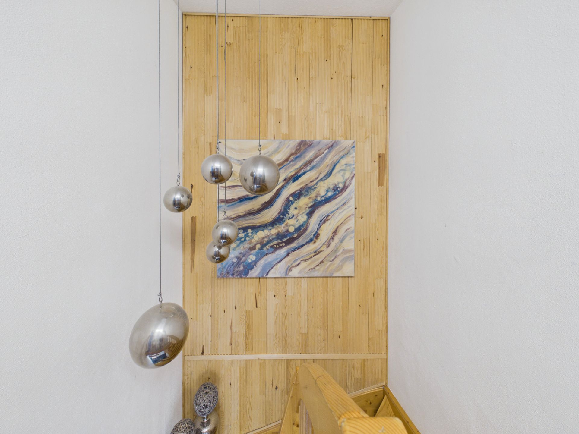 Hölzerne Wand mit abstraktem Gemälde und mehreren silbernen Kugellampen im Treppenhaus.