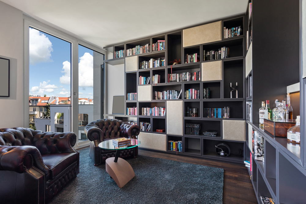 Wohnzimmer mit großen Bücherregalen, zwei Ledersesseln, Glastisch und Balkonblick.
