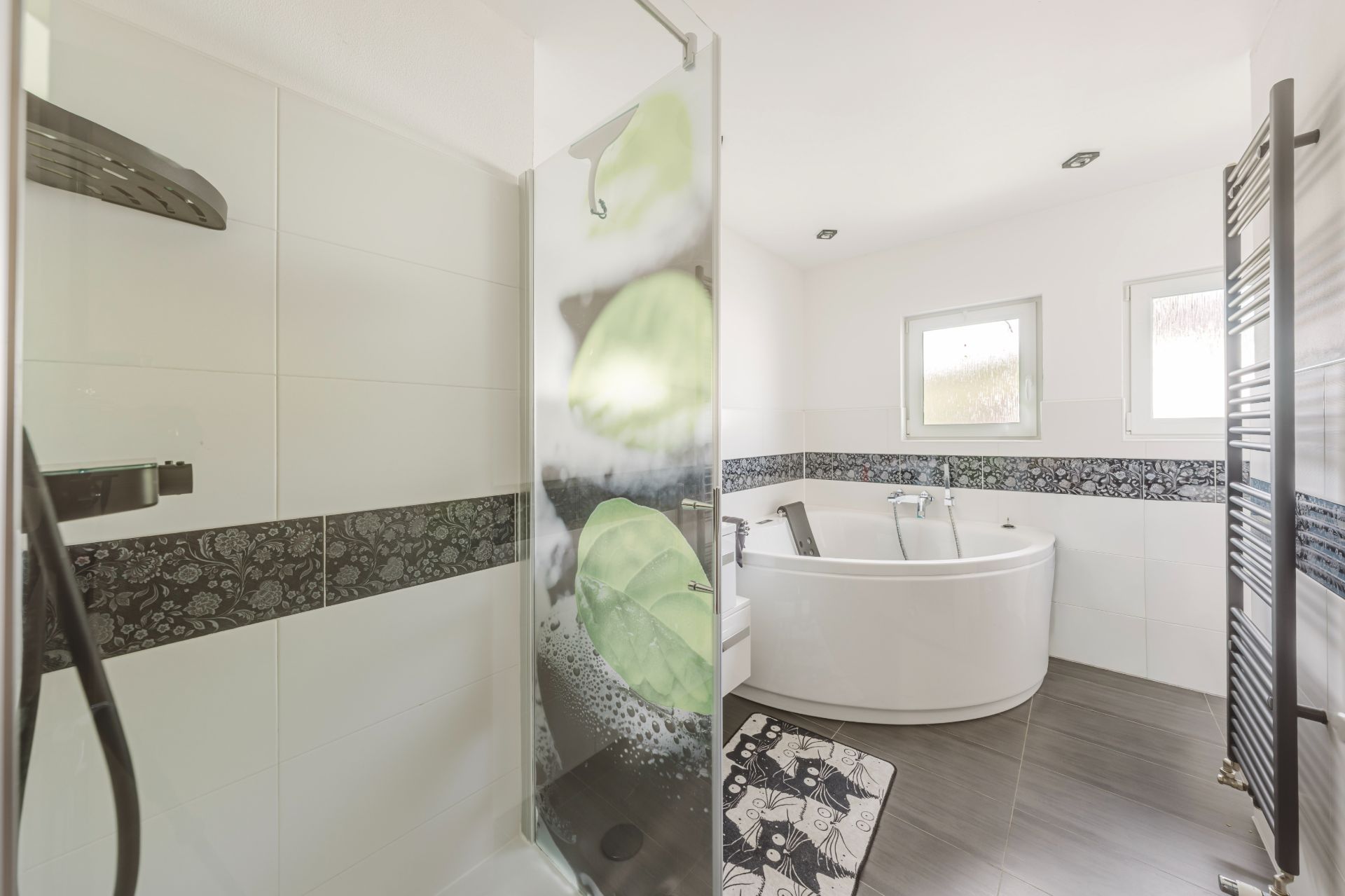 Modernes Badezimmer mit Dusche, Badewanne, zwei Fenstern und Handtuchheizkörper.