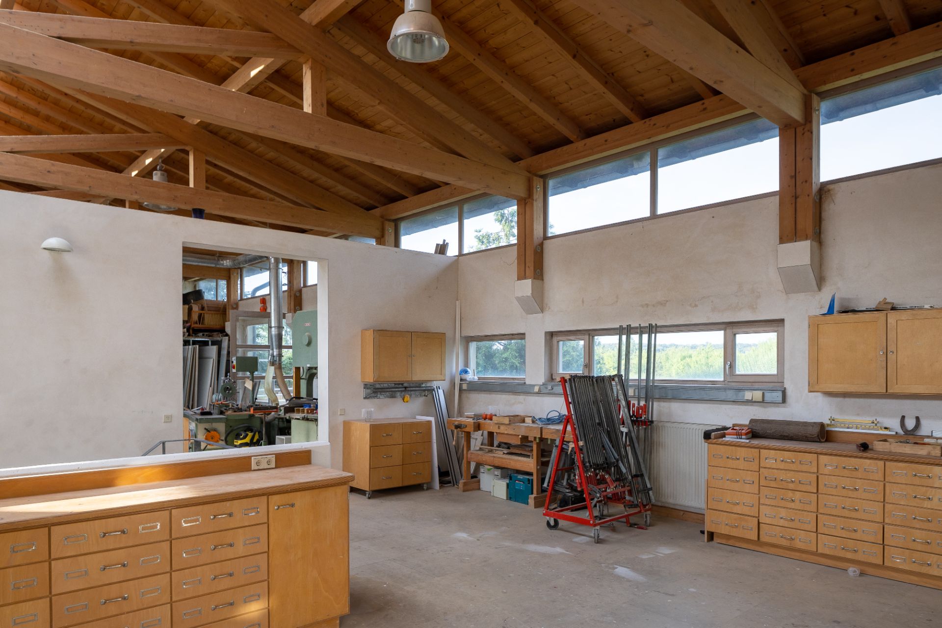 Heller Raum mit Holzdecke, Fenstern und vielen Holzschränken, eingerichtet als Werkstatt.