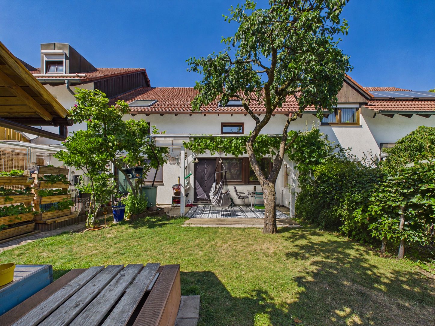 Grüner Garten mit Baum, Terrasse und Sitzbereich vor einem Wohnhaus.
