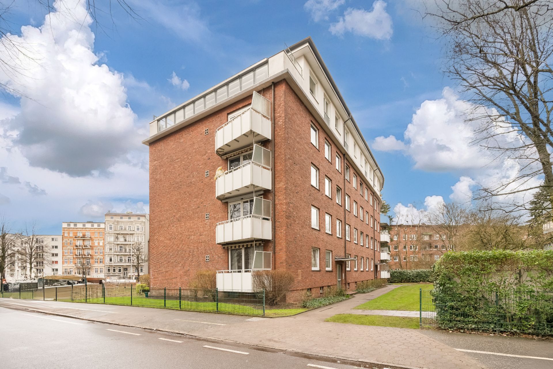 Mehrstöckiges Backsteingebäude mit Balkonen und vielen Fenstern, umgeben von Grünfläche.