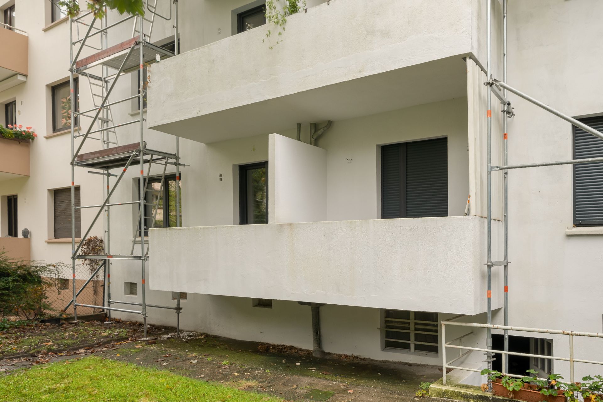 Blick auf einen Balkon mit weißem Geländer und Baugerüst an einer Wohnhausfassade.