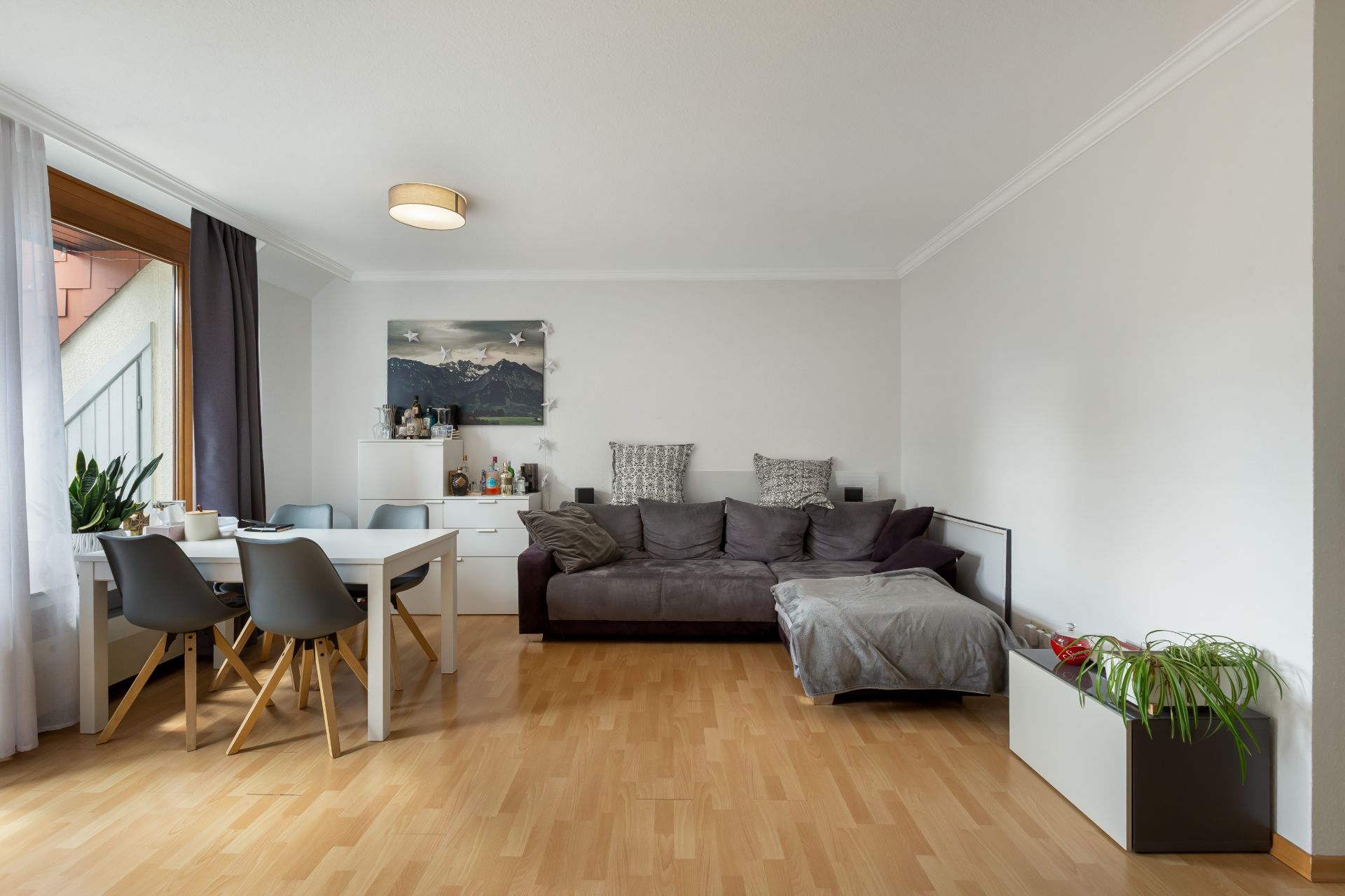 Wohnzimmer mit grauem Sofa, Esstisch, vier Stühlen und Holzboden.