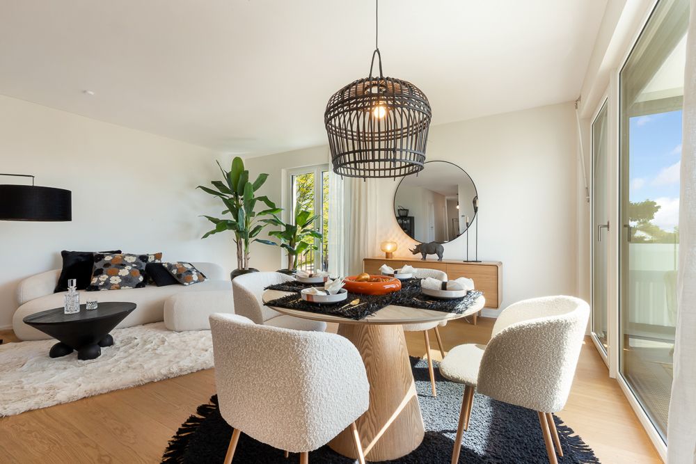 Helles Wohn- und Esszimmer mit rundem Tisch, weißen Stühlen, Sofa und großen Fenstern.