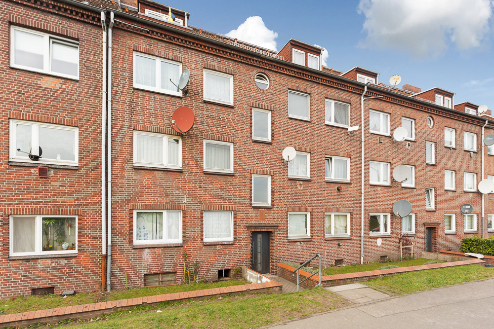 Mehrfamilienhaus aus rotem Backstein mit vielen Fenstern und Satellitenschüsseln an der Fassade.