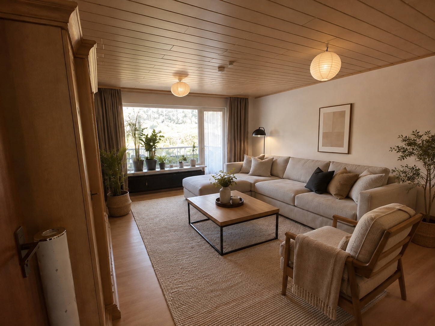 Helles Wohnzimmer mit großem Sofa, Sessel, Couchtisch, Pflanzen und großem Fenster.