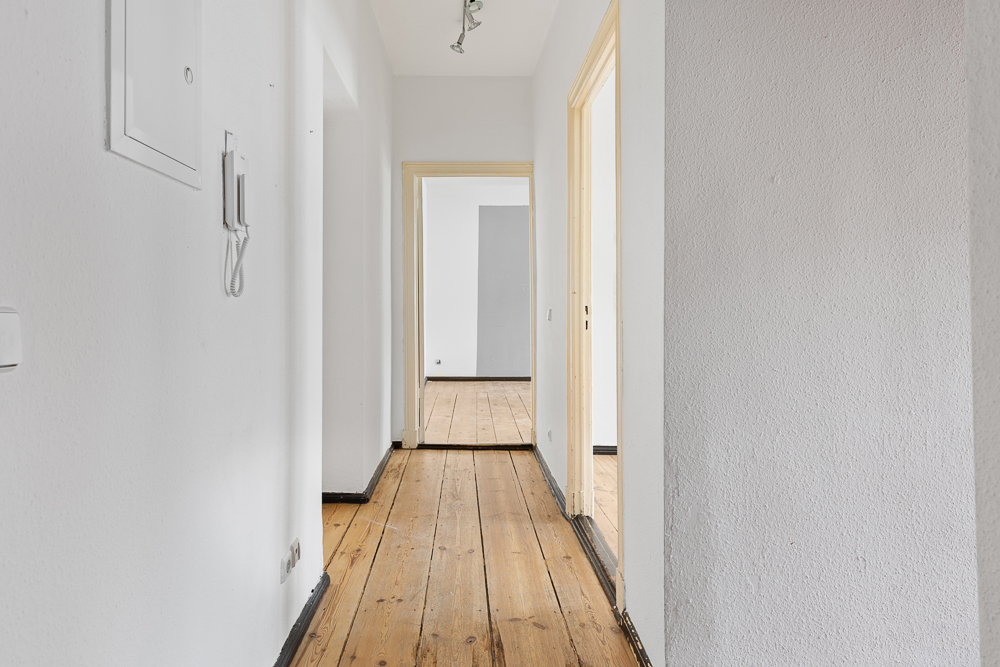Heller Flur mit Holzboden und weißen Wänden, führt zu mehreren Türen.