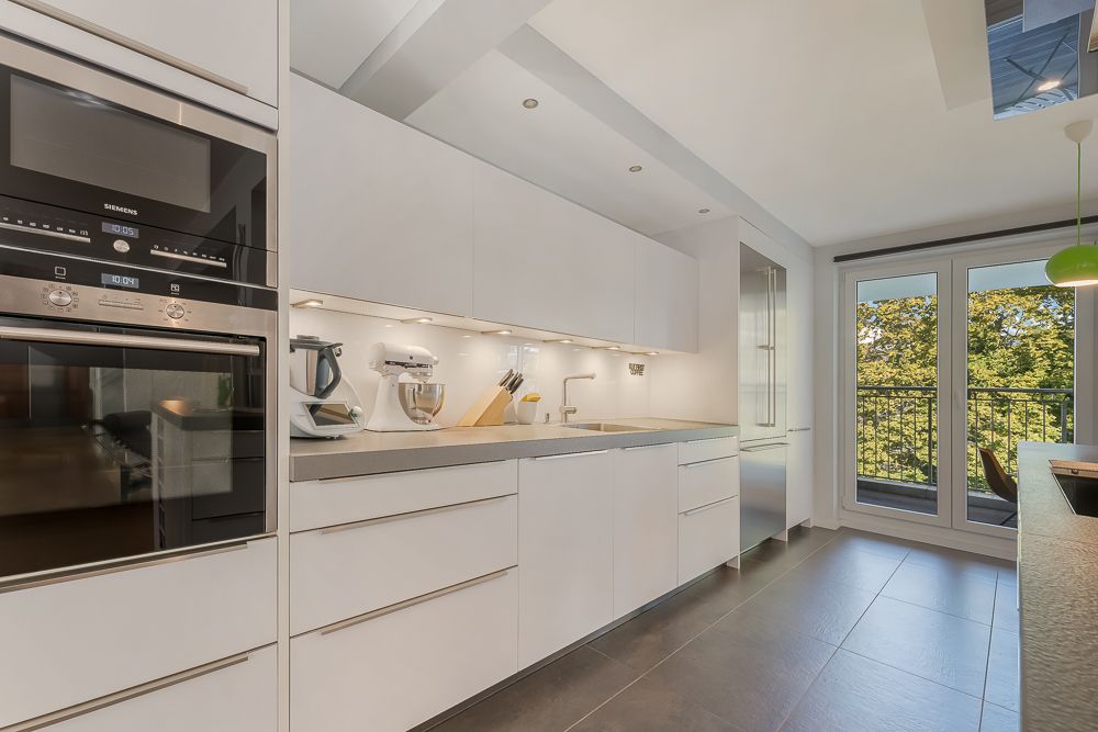 Moderne, helle Küche mit weißen Schränken und großen Fenstern zum Balkon.